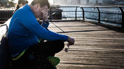 Mann sitzt auf einer Bank und reibt sich die Augen vor Müdigkeit