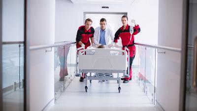 Patient wird im Krankenhausbett durch ein Krankenhaus geschoben