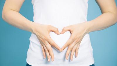 Frau formt mit Ihren Fingern ein Herz vor dem Bauch
