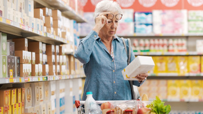 Ältere Frau mit Sehschwäche beim Lesen von Informationen auf einer Produktverpackung im Supermarkt