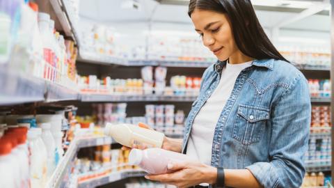 Frau vergleicht im Supermarkt zwei Lebensmittel