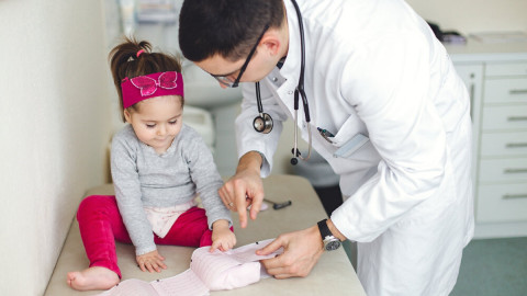 Kleines Mädchen sitzt auf der Behandlungsliege und schaut sich mit dem Arzt ein EKG an