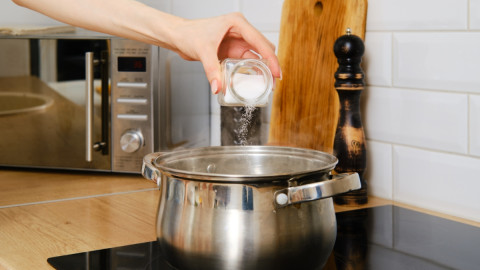 Nahaufnahme einer weiblichen Hand, die Salz in kochendes Wasser gießt