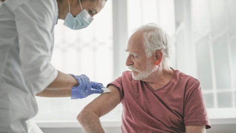 Ärztin mit Handschuhen und Mundschutz impft einen Herzpatienten im Behandlungszimmer. Besonders für Risikogruppen wird die Gürtelrose-Impfung empfohlen.